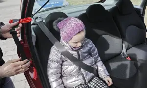 Dziecko w samochodzie, zapinany pas bezpieczeństwa. W tle radiowóz policji. To inteligentne rozwiązanie dla bezpieczeństwa najmłodszych.