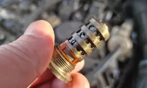 Uszkodzony zawór zmiennych faz rozrządu objawy: brudny, metalowy element z otworami, trzymany w palcach.