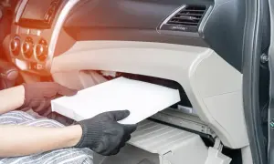Ręce w czarnych rękawiczkach trzymają biały filtr kabinowy, który został odwrotnie założony.