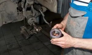 Mechanik trzyma nowe łożysko koła, przygotowując się do wymiany. Pokazuje, jak sprawdzić łożysko w kole.