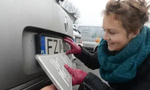 Kobieta w czerwonych rękawiczkach montuje tablicę rejestracyjną. To ważny etap w procesie rejestracji samochodowej.