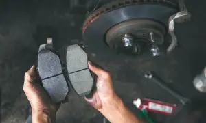 Ręce mechanika porównują zużyte i nowe klocki hamulcowe, pokazując, jak sprawdzić klocki hamulcowe.