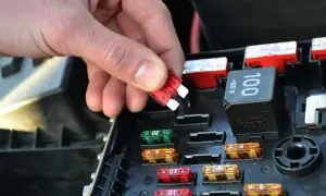 Dłoń wymienia czerwony bezpiecznik w skrzynce bezpieczników Skoda Octavia 2. Widać też inne bezpieczniki i przekaźnik.