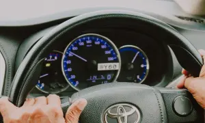 Dłonie na kierownicy Toyoty, widoczne zegary. Trudności ze skręcaniem mogą oznaczać zapowietrzony układ wspomagania objawy.