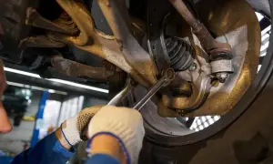 Mechanik w rękawiczkach dokręca śrubę w zawieszeniu samochodu.