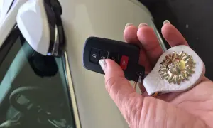 Dłoń trzyma kluczyk, ale auto nie reaguje na kluczyk. Na breloczku ozdoba w kształcie słońca.