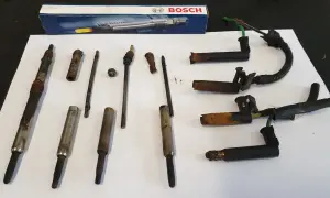 Zestaw skorodowanych świec żarowych, w tym jedna urwana świeca żarowa, obok pudełka Bosch.