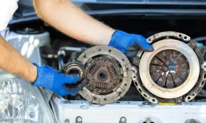 Wymiana sprzęgła krok po kroku: mechanik w niebieskich rękawiczkach trzyma zużyte części.