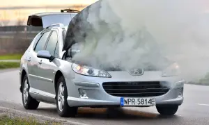 Srebrny Peugeot z otwartą maską i dymem wydobywającym się z silnika. Rozbiegany silnik diesla na poboczu drogi.
