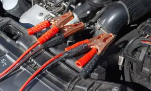 Kable rozruchowe podłączone do akumulatora, bo auto nie odpala. Miedziane klamry i czerwono-czarne uchwyty.