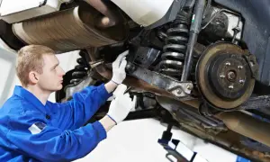 Mechanik w niebieskim kombinezonie sprawdza elementy zawieszenia samochodu, w tym sprężyny i hamulce.