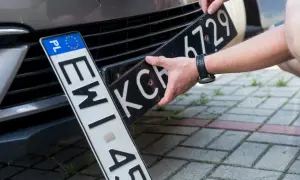 Wymiana tablic rejestracyjnych. Jedna tablica z oznaczeniem PL jest już zamontowana, druga jest wkładana.