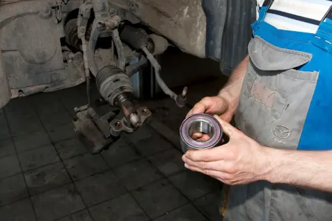 Mechanik trzyma nowe łożysko koła, przygotowując się do wymiany. Pokazuje, jak sprawdzić łożysko w kole.