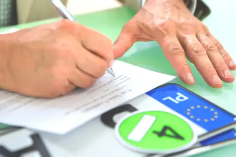 Podpisanie umowy kupna-sprzedaży pojazdu, tuż po rejestracja. Na stole leżą tablice rejestracyjne.