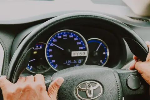 Dłonie na kierownicy Toyoty, widoczne zegary. Trudności ze skręcaniem mogą oznaczać zapowietrzony układ wspomagania objawy.
