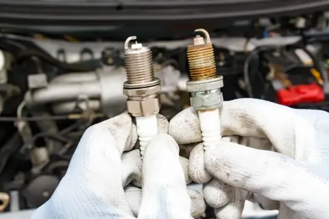 Ręce w białych rękawiczkach trzymają dwie świece zapłonowe, jedną nową, drugą zużytą. Czy diesel ma świece zapłonowe? Nie, diesel nie ma świec zapłonowych.