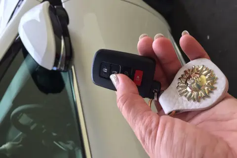 Dłoń trzyma kluczyk, ale auto nie reaguje na kluczyk. Na breloczku ozdoba w kształcie słońca.