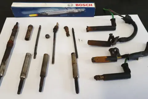 Zestaw skorodowanych świec żarowych, w tym jedna urwana świeca żarowa, obok pudełka Bosch.