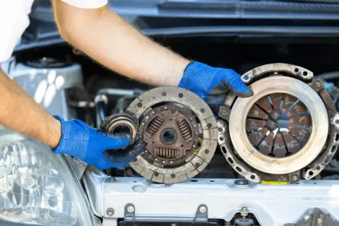 Wymiana sprzęgła krok po kroku: mechanik w niebieskich rękawiczkach trzyma zużyte części.
