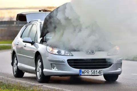 Srebrny Peugeot z otwartą maską i dymem wydobywającym się z silnika. Rozbiegany silnik diesla na poboczu drogi.