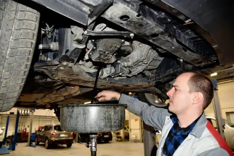 Mechanik spuszcza olej z silnika. Pamiętaj, co ile wymiana oleju jest kluczowa dla żywotności auta.