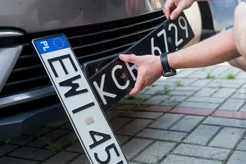 Wymiana tablic rejestracyjnych. Jedna tablica z oznaczeniem PL jest już zamontowana, druga jest wkładana.