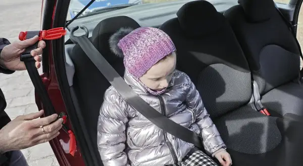Dziecko w samochodzie, zapinany pas bezpieczeństwa. W tle radiowóz policji. To inteligentne rozwiązanie dla bezpieczeństwa najmłodszych.