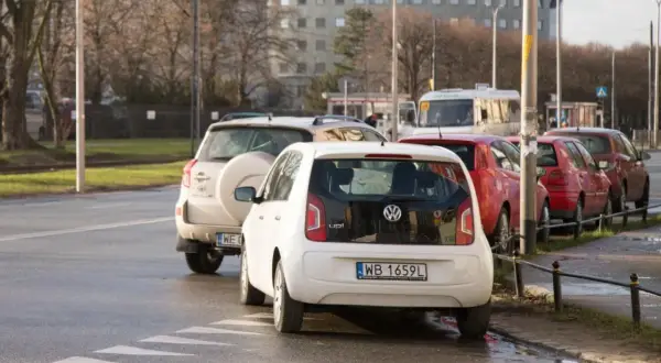 Biały Volkswagen Up i inne samochody stoją na pasach, blokując skrzyżowanie.