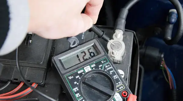 Pomiar napięcia multimetrem na akumulatorze samochodowym. Wynik 12.6V pokazuje, jak sprawdzić akumulator.