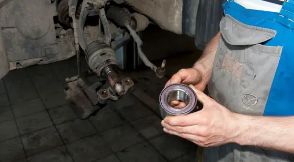 Mechanik trzyma nowe łożysko koła, przygotowując się do wymiany. Pokazuje, jak sprawdzić łożysko w kole.