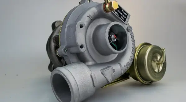 Metalowa turbosprężarka, potencjalnie z objawami uszkodzonej turbiny. Widoczny wirnik i zawór upustowy.