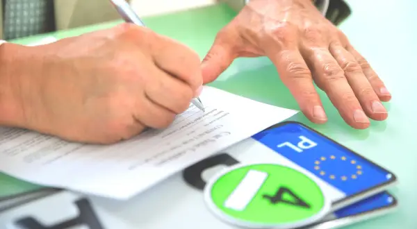 Podpisanie umowy kupna-sprzedaży pojazdu, tuż po rejestracja. Na stole leżą tablice rejestracyjne.