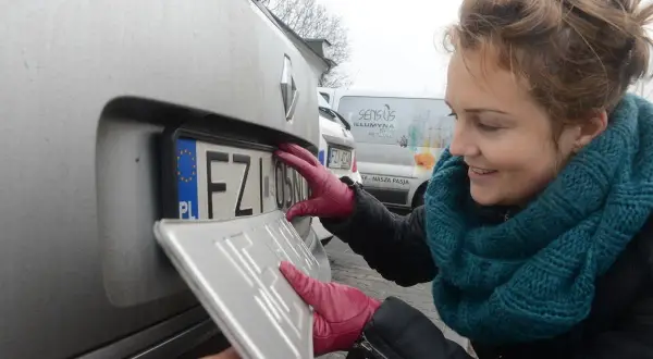 Kobieta w czerwonych rękawiczkach montuje tablicę rejestracyjną. To ważny etap w procesie rejestracji samochodowej.
