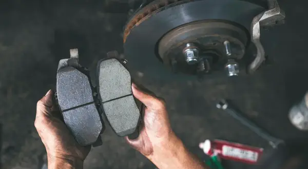 Ręce mechanika porównują zużyte i nowe klocki hamulcowe, pokazując, jak sprawdzić klocki hamulcowe.