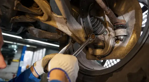Mechanik w rękawiczkach dokręca śrubę w zawieszeniu samochodu.