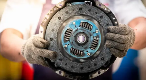 Mechanik trzyma w rękawicach odwrotnie założoną tarczę sprzęgła, gotową do montażu.