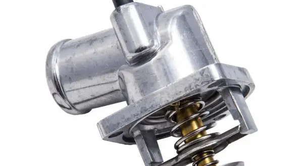 Metalowy termostat w samochodzie, kluczowy element układu chłodzenia, z widoczną sprężyną i zaworem.
