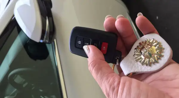 Dłoń trzyma kluczyk, ale auto nie reaguje na kluczyk. Na breloczku ozdoba w kształcie słońca.