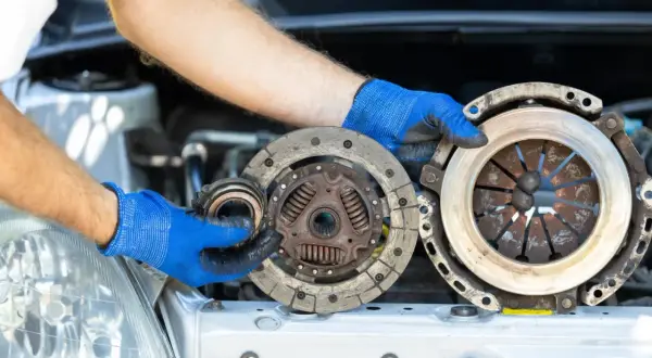 Wymiana sprzęgła krok po kroku: mechanik w niebieskich rękawiczkach trzyma zużyte części.