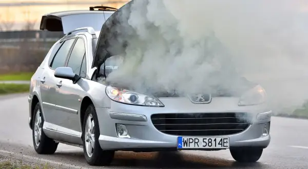 Srebrny Peugeot z otwartą maską i dymem wydobywającym się z silnika. Rozbiegany silnik diesla na poboczu drogi.