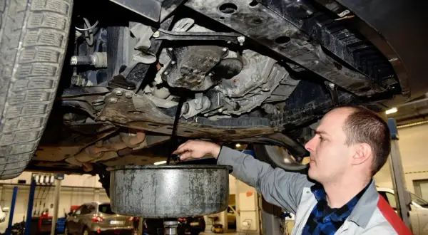 Mechanik spuszcza olej z silnika. Pamiętaj, co ile wymiana oleju jest kluczowa dla żywotności auta.
