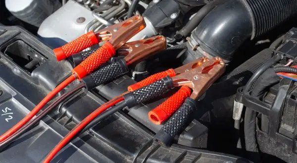 Kable rozruchowe podłączone do akumulatora, bo auto nie odpala. Miedziane klamry i czerwono-czarne uchwyty.