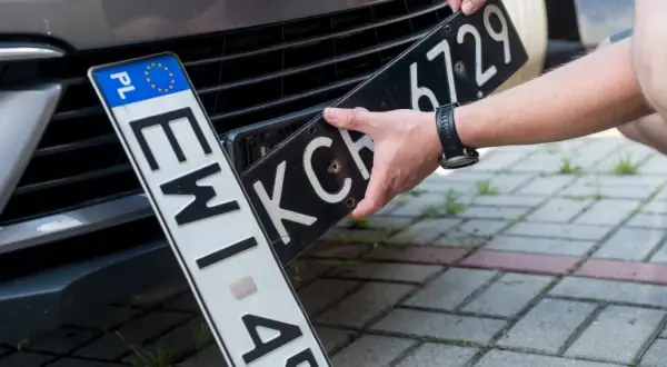Wymiana tablic rejestracyjnych. Jedna tablica z oznaczeniem PL jest już zamontowana, druga jest wkładana.