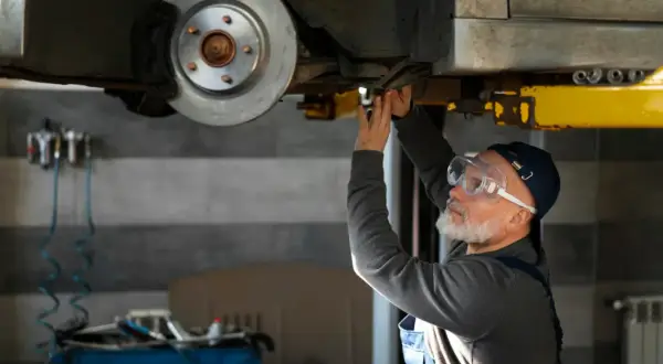 Mechanik w okularach ochronnych pracuje pod samochodem, być może szukając sposobu, jak odblokować hamulec ręczny elektryczny.