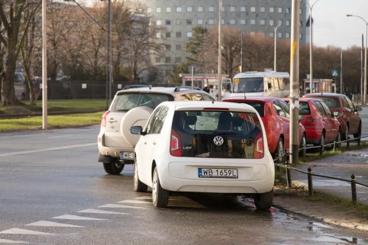 Biały Volkswagen Up i inne samochody stoją na pasach, blokując skrzyżowanie.