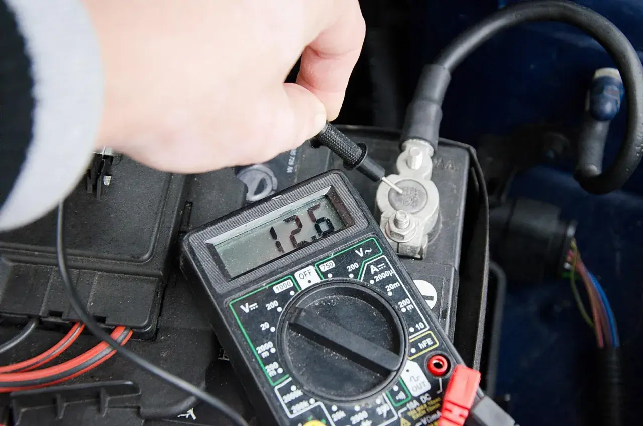 Pomiar napięcia multimetrem na akumulatorze samochodowym. Wynik 12.6V pokazuje, jak sprawdzić akumulator.