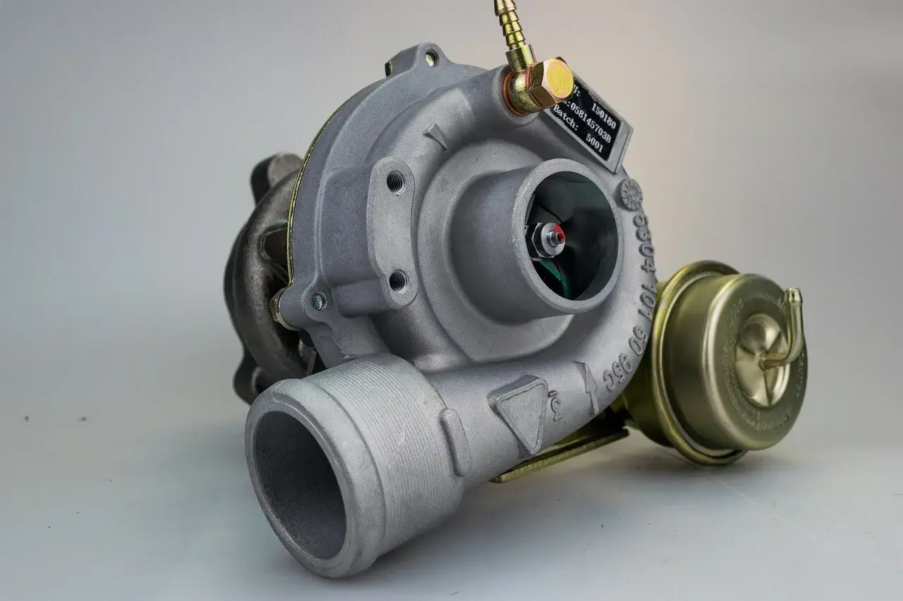 Metalowa turbosprężarka, potencjalnie z objawami uszkodzonej turbiny. Widoczny wirnik i zawór upustowy.