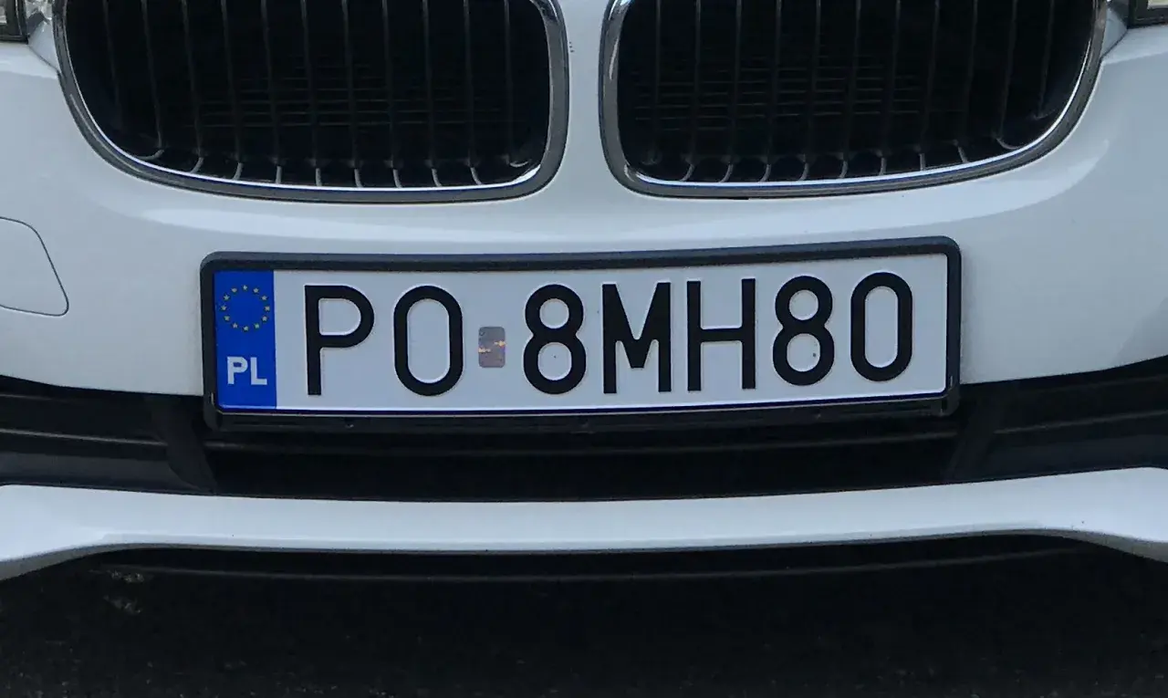 Białe tablice rejestracyjne e.g. PO 8MH80 na zderzaku samochodu.