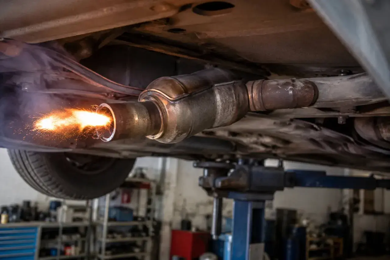 Intensywne płomienie i iskry wydobywające się z rury wydechowej samochodu na podnośniku. To może być proces wypalania DPF na postoju, który trwa różnie.