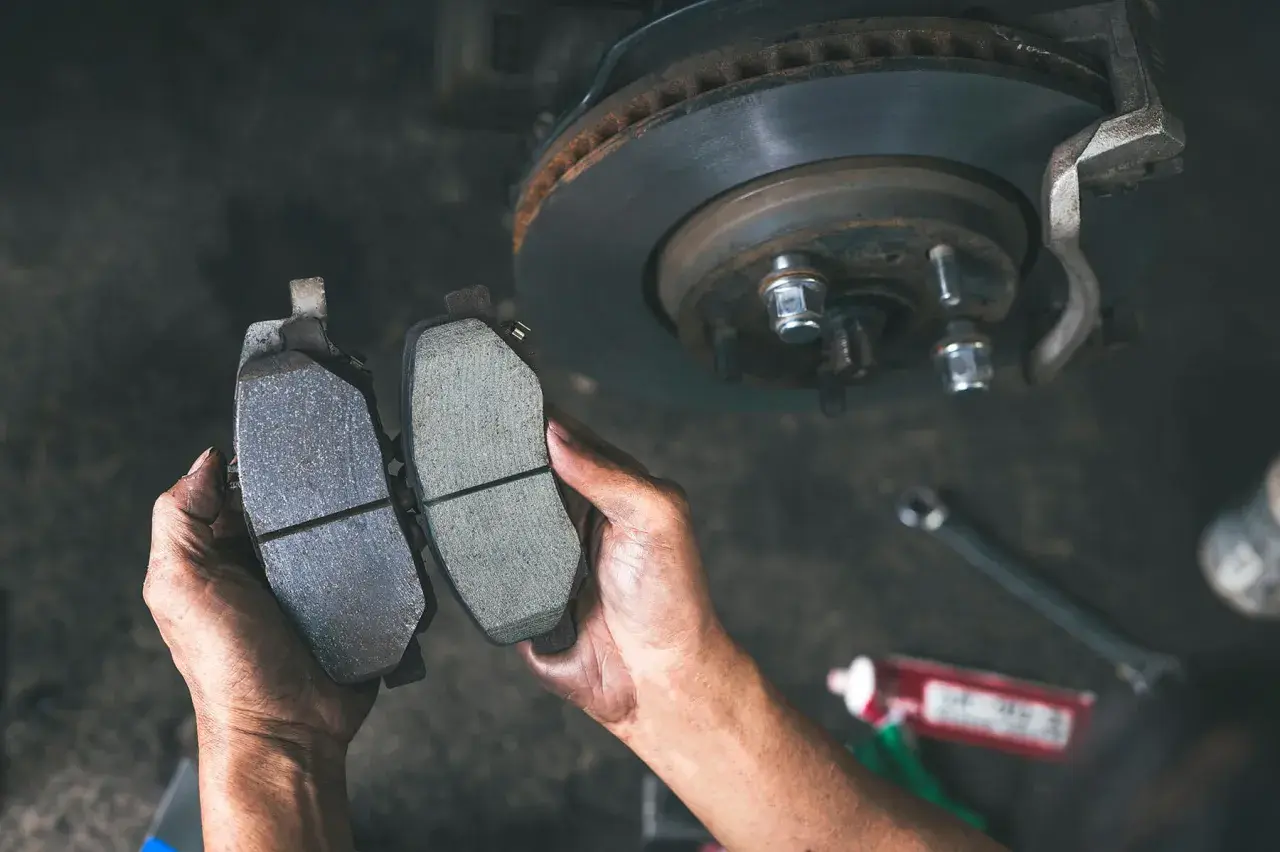 Ręce mechanika porównują zużyte i nowe klocki hamulcowe, pokazując, jak sprawdzić klocki hamulcowe.